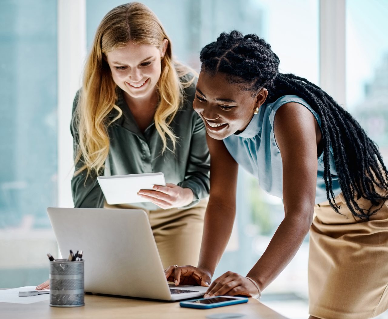 women at computer Two diverse businesswomen working together on a digital tablet and laptop in an office